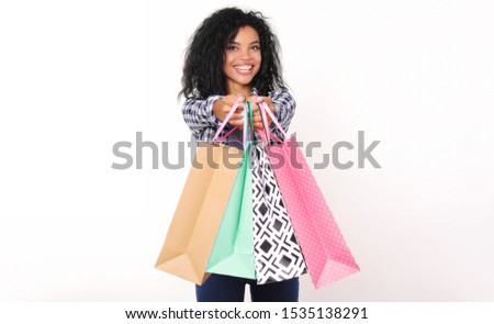 Prices slashed! Beautiful African American woman with outstanding smile is holding four shopping bags in her hands, showing them at the camera.