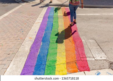 Pride Colors Paint Covers The Crosswalk. A Woman Crosses On The Gay Pride Path Of The Intersection.