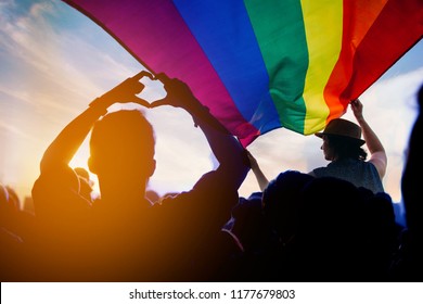 Pride community at a parade with hands raised and the LGBT flag. 