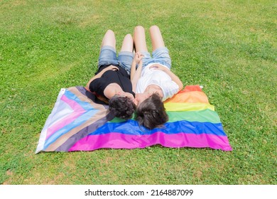 Pride Month. Lesbian Couple On Pride Day. Queer Couple Kissing And Laying On Grass On The Lgbtiq+ Flag.