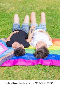 Pride Month. Lesbian Couple On Pride Day. Queer Couple Holding Hands And Laying On Grass On The Lgbtiq+ Flag.