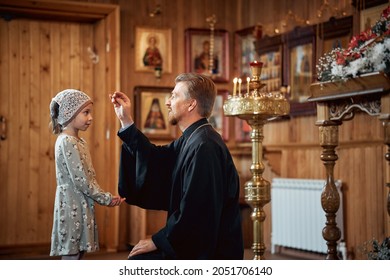 a priest blesses a little girl in a headscarf in an Orthodox church after a festive church mass. - Shutterstock ID 2051706140
