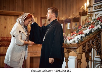 a priest blesses a young woman in a headscarf in an Orthodox church after a festive church mass.
