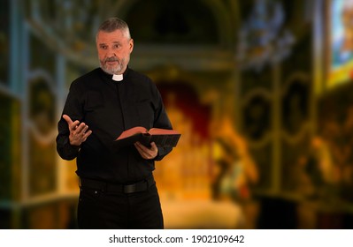 A priest has a Bible in hand and is giving a sermon. He stands in front of an altar. The older man has gray hair and is wearing a black shirt with a white clerical collar.