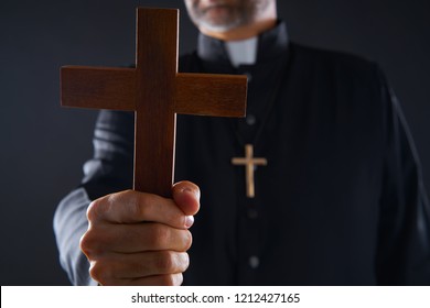 Priest holding cross of wood praying in foreground - Shutterstock ID 1212427165