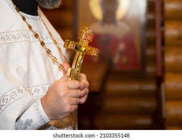 The priest of the Orthodox Church holds a golden cross. A golden cross in the hands of a priest. A male priest holds a large Orthodox cross.