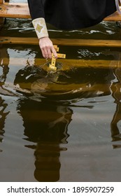 The Priest Performs The Rite Of Water Baptism. Consecration Of Water On The Eve Of The Feast Of The Epiphany. Cross Dipped In Water Close-up, Selective Focus