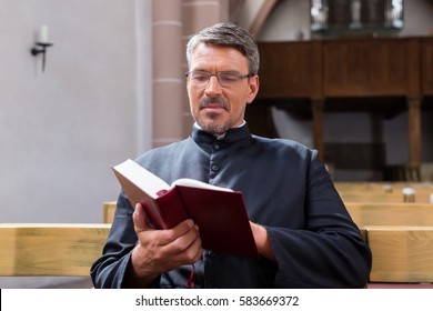 Priest Sitting In Church Reading The Bible