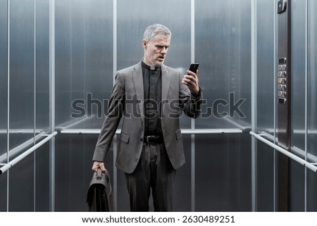 Priest standing in an elevator and checking messages on his smartphone, he is angry and disappointed