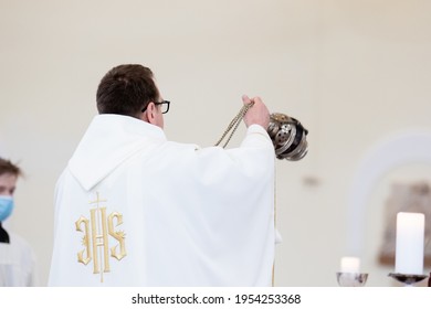 A priest in white liturgical vestments censes with a censer at the altar