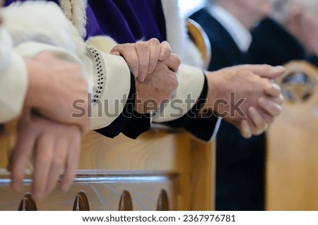 Priests in ceremonial robes clasp their hands in prayer.