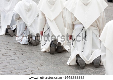 Priests or monks in white cassocks, habits with rosaries kneeling on the ground. Christianity, faith calling and spirituality, catholic monks kneeling on the street in prayer concept