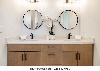 primary bathroom with brown wood cabinets round mirrors glass wall shower walk in closet hardwood floors dark metal fixtures - Shutterstock ID 2285337061