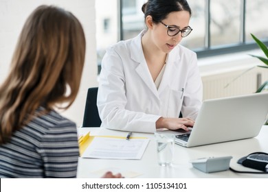 Primary Care Physician Typing On Laptop Useful Observations While Listening To Her Female Patient In The Office Of A Modern Medical Center 