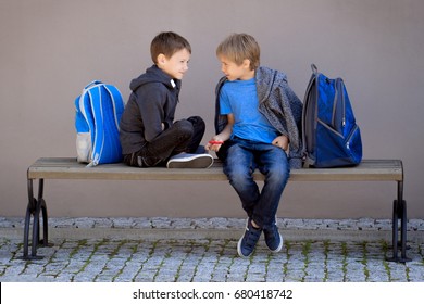 Primary education, school, friendship concept - two boys with backpacks sitting, talking and playing with spinner after school