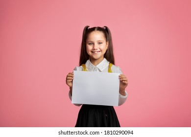 Primary education. Small schoolgirl with happy smile holding sign with free space, isolated on pink background, studio shoot - Powered by Shutterstock