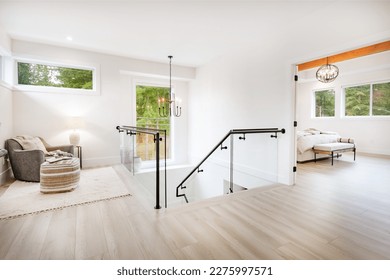 Primary master bedroom with wood beam ceiling hardwood floors white walls sitting area with comfortable chair and books on shelves near staircase with glass walls and wrought iron rails upstairs rooms - Shutterstock ID 2275997571