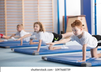 Primary school boy and other kids exercising a balancing table yoga pose during extracurricular gym class to help with posture and core body strength - Powered by Shutterstock