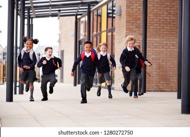 Primary school kids, wearing school uniforms and backpacks, running on a walkway outside their school building, front view - Shutterstock ID 1280272750