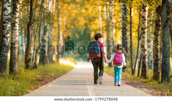 Primary school pupil. boy and girl with backpacks\
walking down street. Happy children happy to go back to school.\
beginning school year. Children in full growth, with joy went to\
school. rear view