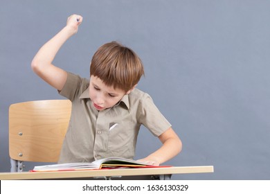 A primary school student is doing homework. The child at the desk with the textbook is angry. The boy does not want to study. A seven-year-old child goes crazy for lessons. - Powered by Shutterstock