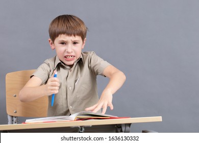 A primary school student is doing homework. The child at the desk with the textbook is angry. The boy does not want to study. A seven-year-old child goes crazy for lessons. - Powered by Shutterstock