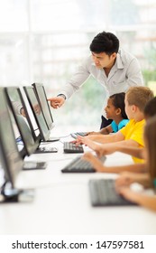 Primary School Teacher Helping Student In Computer Room