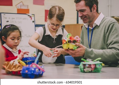 Primary school teacher is helping two of his students with a STEM project. They are building something using recycled items and crafts equipment.  - Powered by Shutterstock