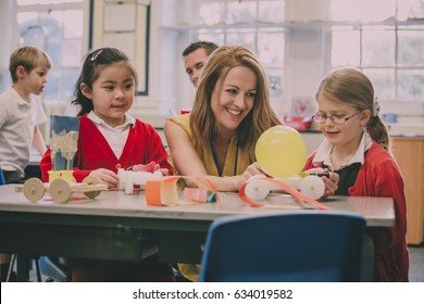 Primary school teacher is helping two of her students with a STEM project. They are building something using recycled items and crafts equipment.  - Powered by Shutterstock