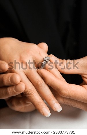 Prime adult Asian male putting engagement ring on female-s hand.