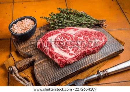 Prime Raw wagyu Rib Eye beef meat steak on wooden board. Orange background. Top view.