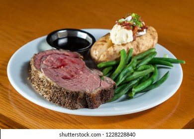 Prime Rib Meal Served On A Plate With A Loaded Potato And Green Beans With A Side Of A Jus