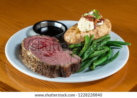 prime rib meal served on a plate with a loaded potato and green beans with a side of a jus