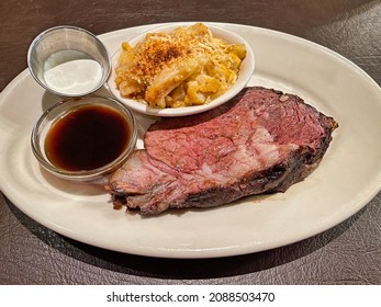 A Prime Rib Stake With Au Gratin Potatoes And Dipping Sauces On The Side.