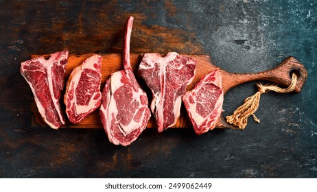 Prime steaks Black Angus on a wooden board: Tomahawk steak, Ribeye, T-bone and Ossobuco. A set of steaks for grilling. Top view. - Powered by Shutterstock