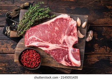 Prime T-bone beef meat steak, raw porterhouse steak on butcher board with herbs. Wooden background. Top view. - Powered by Shutterstock