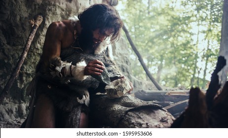 Primeval Caveman Wearing Animal Skin Hits Rock with Sharp Stone and Makes First Primitive Tool for Hunting Animal Prey or to Handle Hides. Neanderthal Using Handax. Dawn of Human Civilization