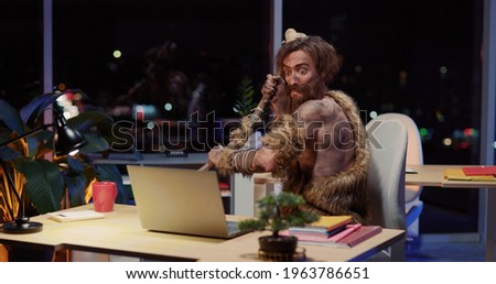 Primeval IT engineer using laptop computer discovering technology at modern database. Happy savage neanderthal dancing with joy having fun staying at data center.