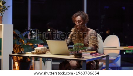 Primeval IT engineer using laptop computer discovering technology at modern database. Happy savage neanderthal dancing with joy having fun staying at data center.