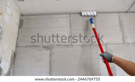 Priming the wall with a roller, apartment renovation concept. A man paints a wall with a roller. A man builder priming a wall before doing further work with a construction roller.
