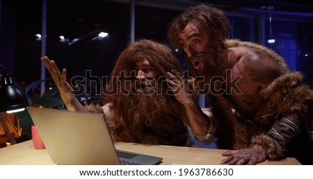Primitive neanderthal people couple traveling through time working in contamporary office playing woith gagdets interacting new things.