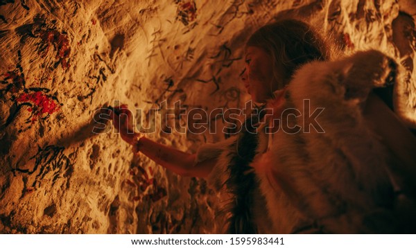 Primitive Prehistoric Neanderthal Child Wearing\
Animal Skin Draws Animals and Abstracts on the Walls at Night.\
Creating First Cave Art with Petroglyphs, Rock Paintings\
Illuminated by Fire. Low\
Angle