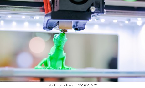Print head of 3D printer machine printing plastic model of green toy lizard at modern scifi technology exhibition. 3D printing, additive technologies, 4.0 industrial revolution and futuristic concept