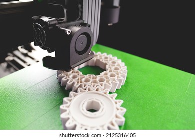 print head, bright green print bed and white helical gears with visible infill and layer. opblique view on process of 3D-printing. copy space for text. selective focus. additive manufacturing concept - Shutterstock ID 2125316405