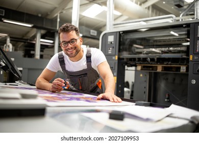 Print house worker controlling printing process quality and checking colors with magnifying glass.