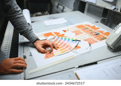 Print house worker controlling printing process quality and checking colors with magnifying glass.