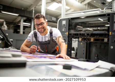 Print house worker controlling printing process quality and checking colors with magnifying glass.