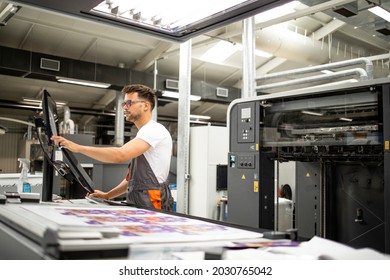 Print house worker setting parameters on modern offset printing machine.