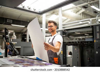 Print shop worker checking quality of imprint and controlling printing process.