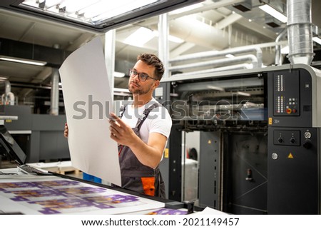 Print shop worker checking quality of imprint and controlling printing process.